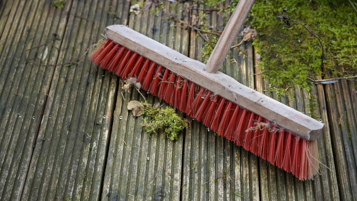 mit einem roten Besen wird eine Holzterrasse gereinigt