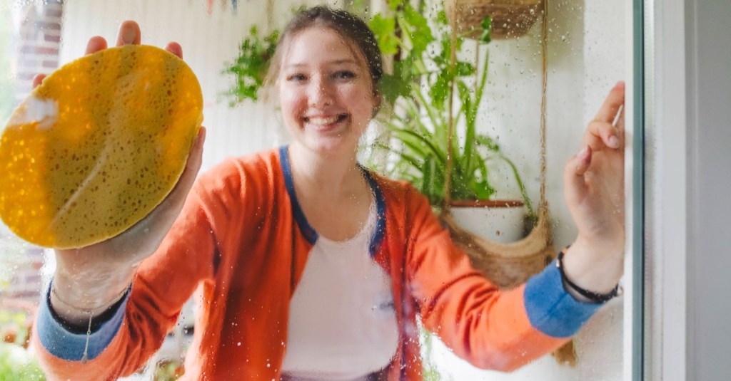 Cleanfluencer: eine junge Frau putzt ihre Fenster und lächelt in die Kamera