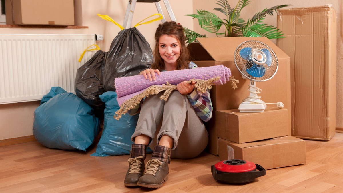 Eine Frau sitzt in ihrer ausgeräumten Wohnung zwischen Kartons und Müllsäcken.