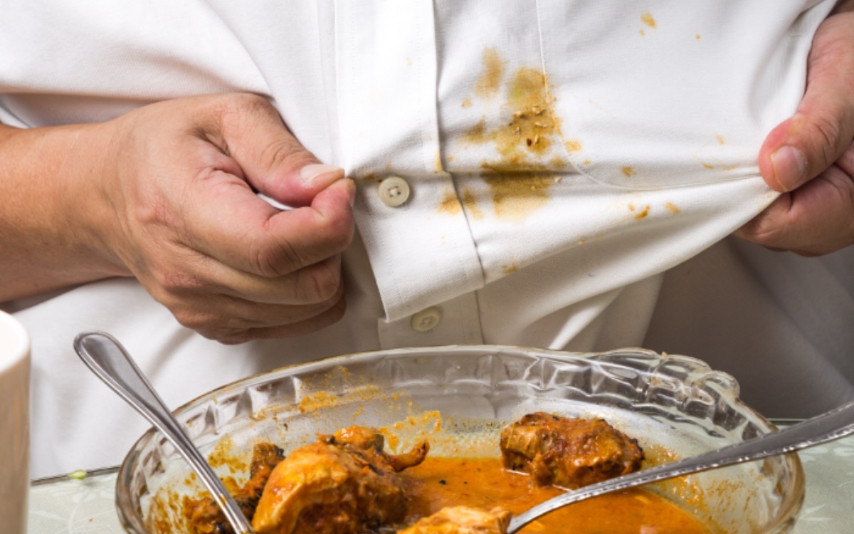 Konzeptbild: Curryfleck entfernen. Ein gelber Curryfleck auf dem Hemd eines Mannes.