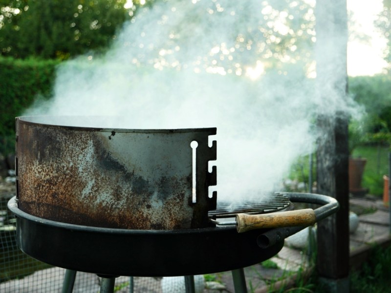 Ein rauchender Grill in einem Garten. Konzeptbild zur Frage: Ist Grillen im Garten erlaubt?