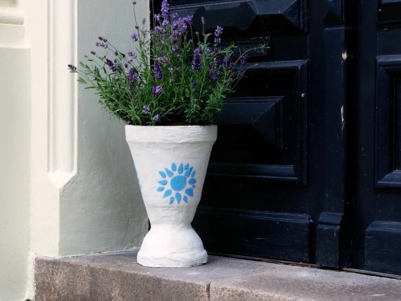 Ein weißer Pflanzenkübel, der mit Lavendel bepflanzt wurde, steht vor einer schwarzen Haustür.