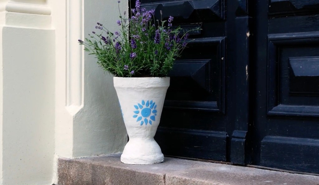 Ein weißer Pflanzenkübel, der mit Lavendel bepflanzt wurde, steht vor einer schwarzen Haustür.