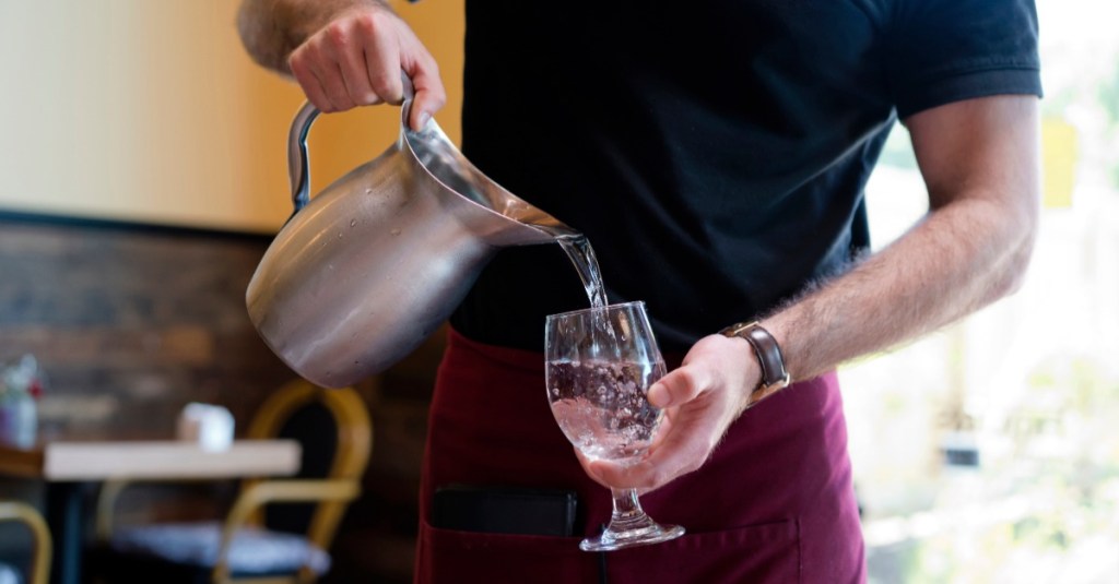 Restaurantbesuch: ein Kellner gießt Wasser in ein Glas